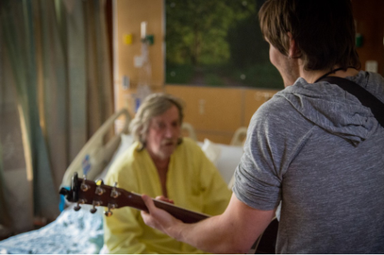 Musicians with guitar performs for hospital patient at bedside